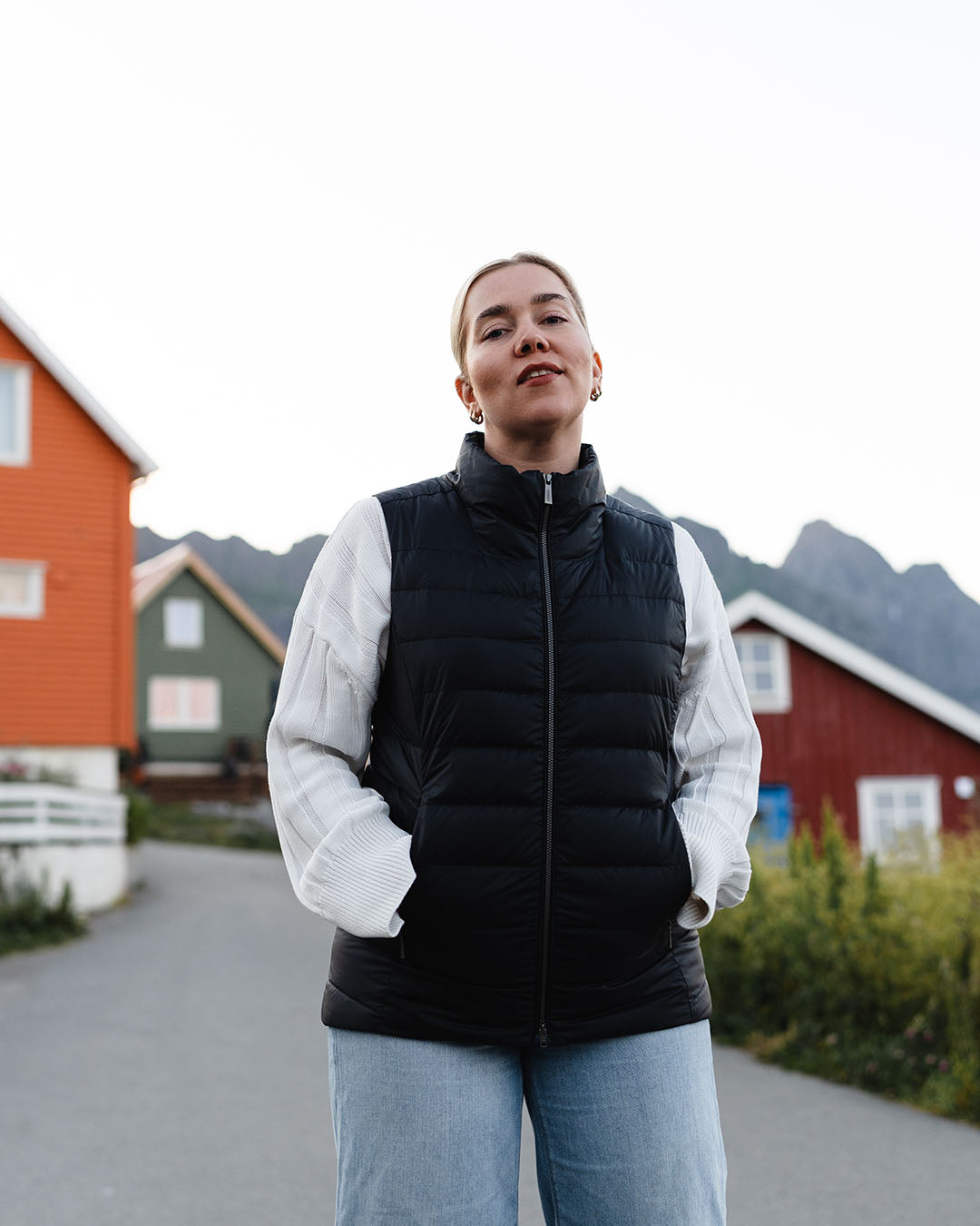 Nainen seisoo kalastajakylässä ja katsoo kameraan. Hänellä on yllään vaakatikattu musta Lady-untuvaliivi (väri: hiilenmusta), valkoinen neule ja vaaleansiniset farkut.