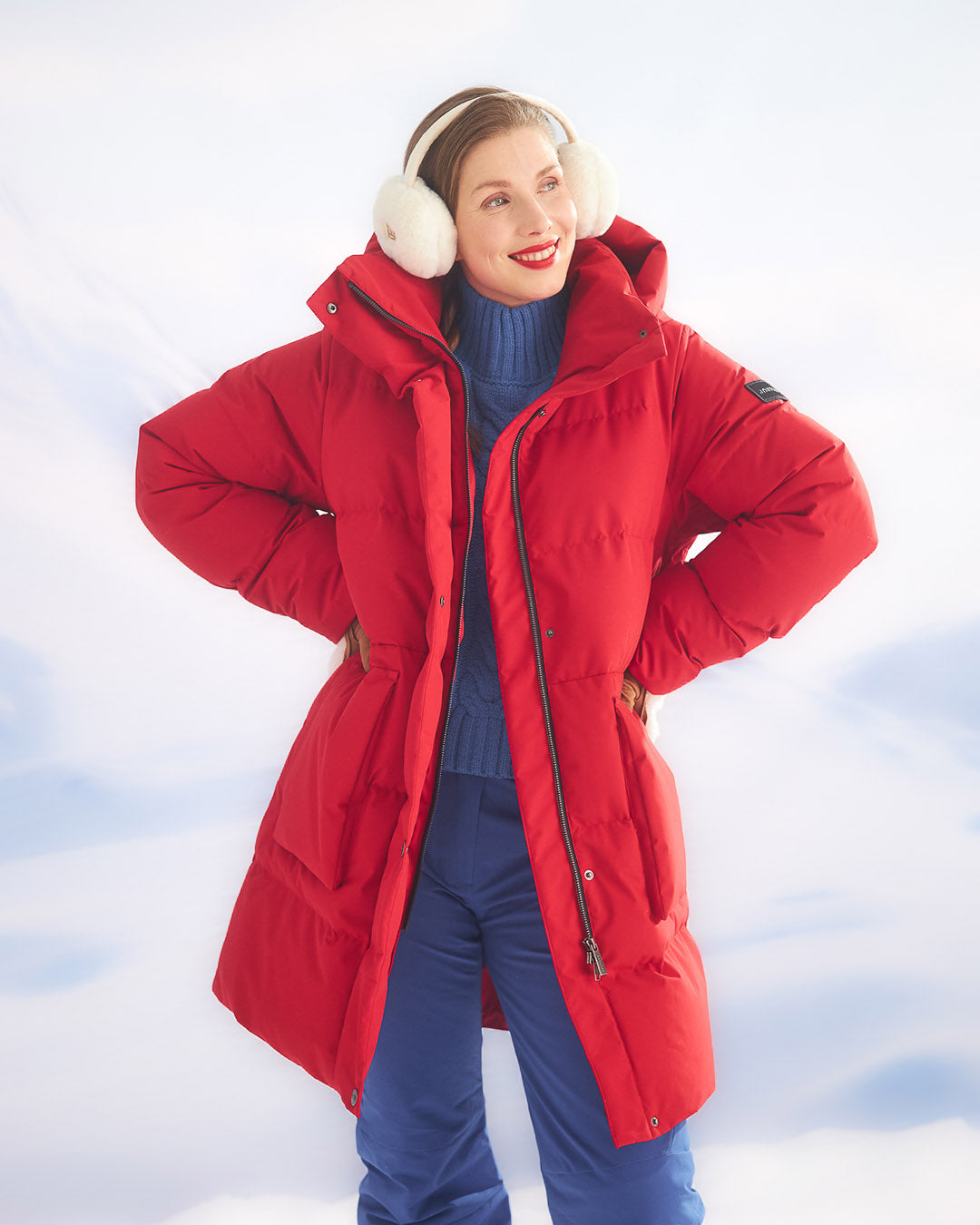 Nainen seisoo lumisessa maisemassa pukeutuneena punaiseen (väri: chili) Siiri-untuvaparkatakkiin. Takki on pitkä ja varustettu suurella hupulla sekä vetoketju- ja painonappikiinnityksellä. Asusteena hänellä on valkoiset korvaläpät ja siniset toppahousut.