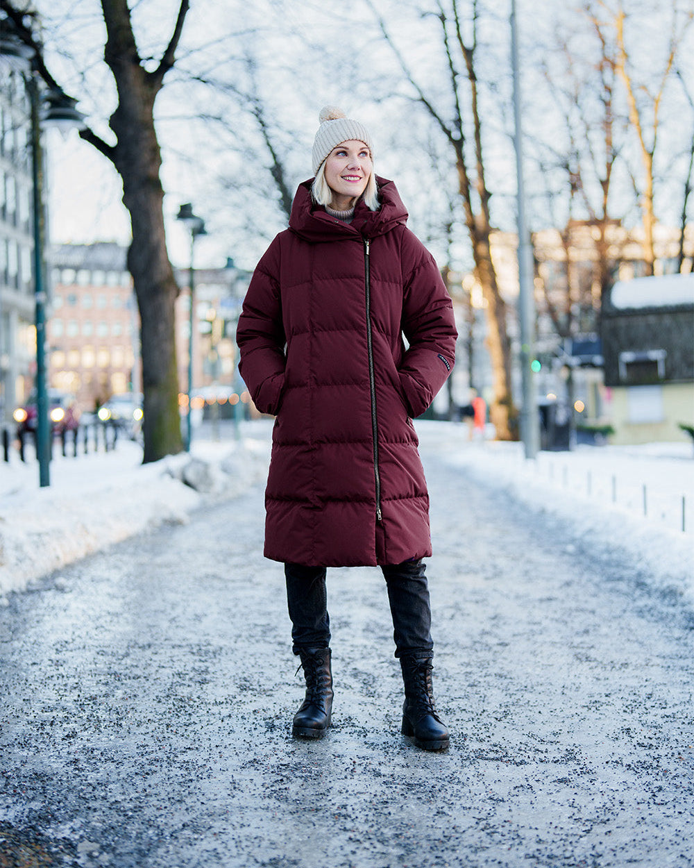 Pitkä, luumunpunainen Lovisa-untuvatakki. Takissa on mattapintainen kangas, leveät vaakasuuntaiset tikkaukset, suuri muhkea huppu ja vetoketju, joka sulkeutuu epäsymmetrisesti kauluksen kohdalla.