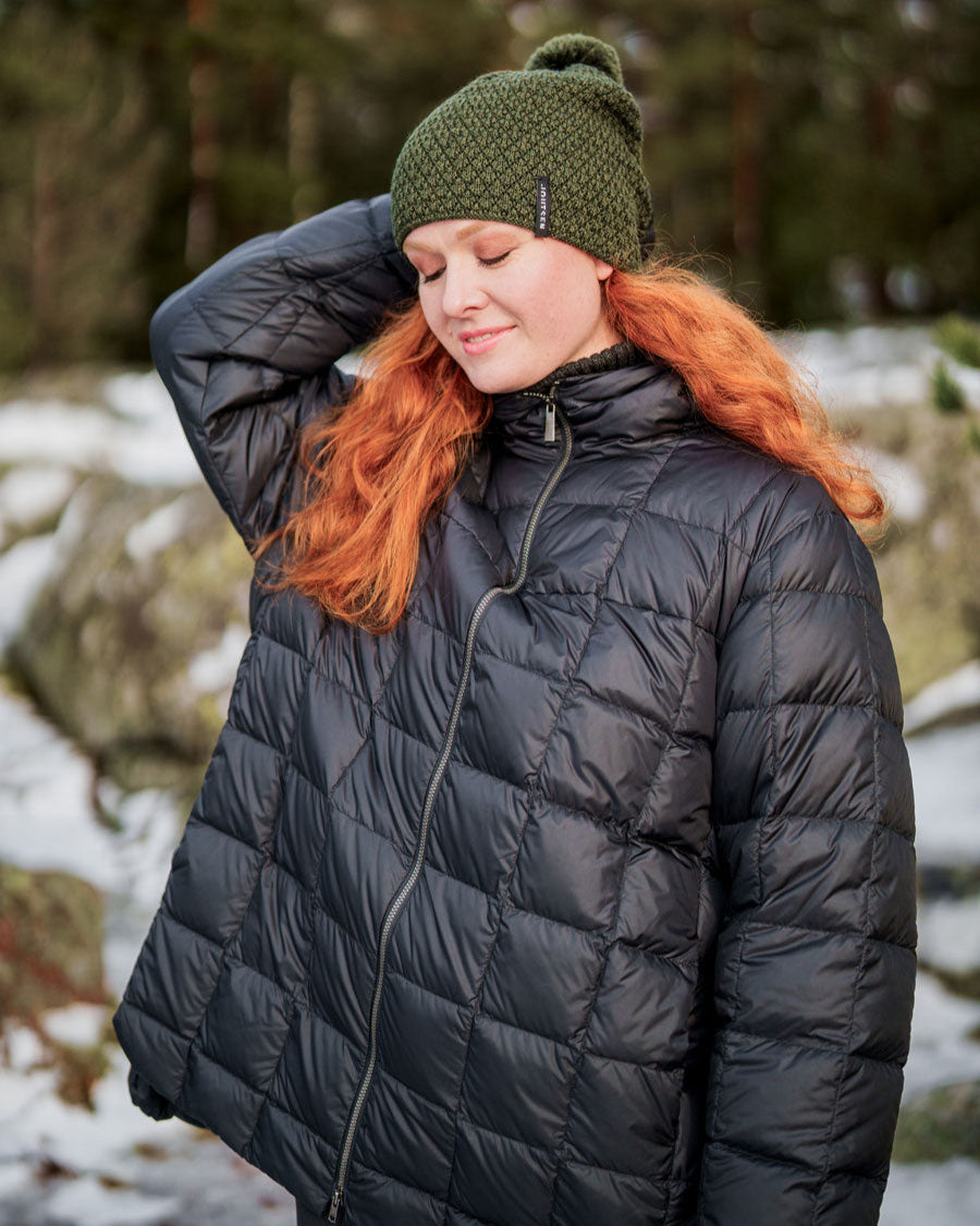 Nainen seisoo ulkona lumisessa maisemassa yllään musta Tulppaani-kevytuntuvatakki (väri: hiilenmusta), jossa on ruututikkaus ja vetoketjukiinnitys. Takissa on kevyt A-linjainen leikkaus.