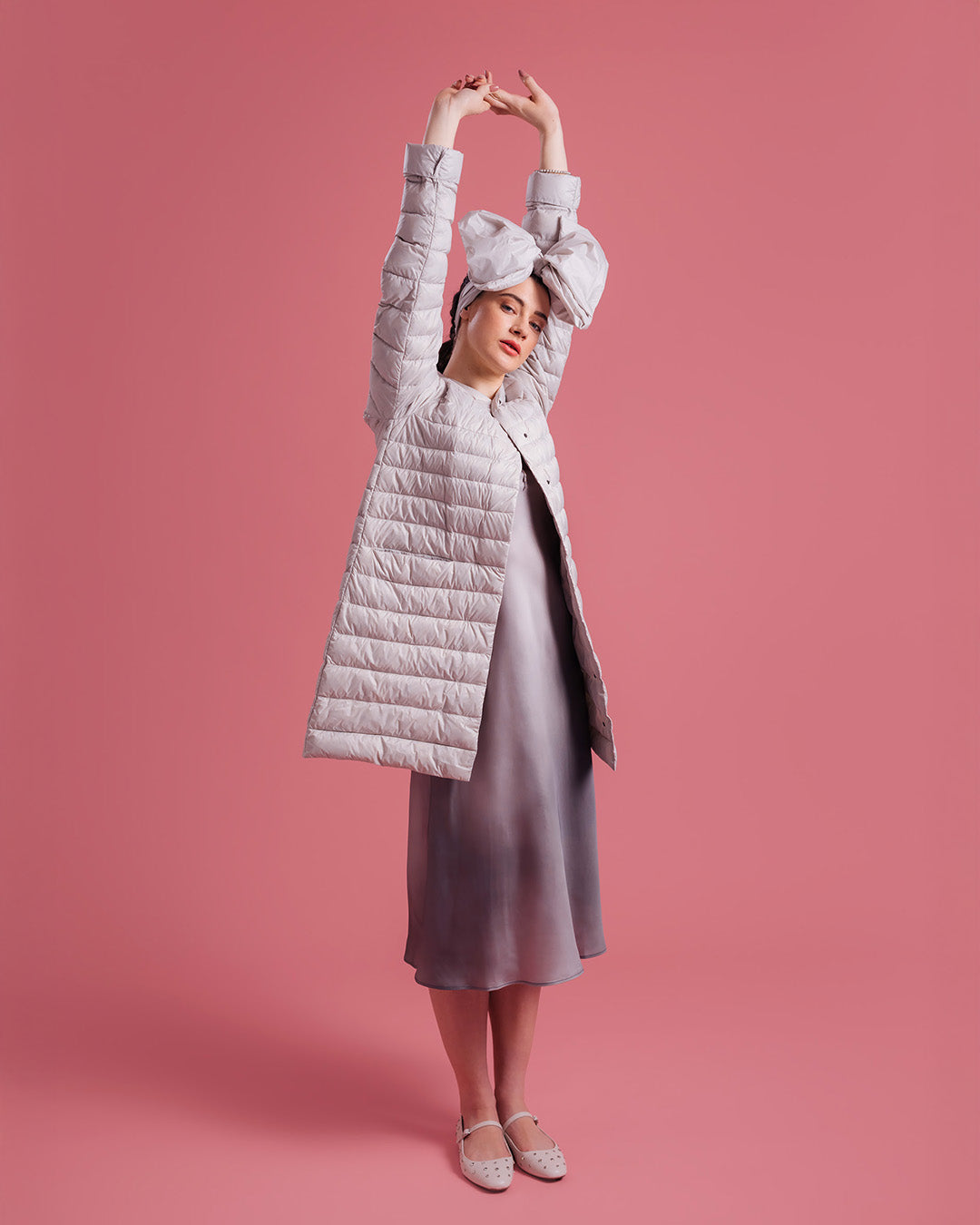 Nainen seisoo vaaleanpunaisella taustalla kädet ylös ojennettuina, pukeutuneena vaaleaan, polvipituiseen Vuokko-kevytuntuvatakkiin (väri: sokeripilvi), hohtavaan liukuvärjättyyn mekkoon ja vaaleisiin kengissä. Asua täydentää suuri rusettipanta.