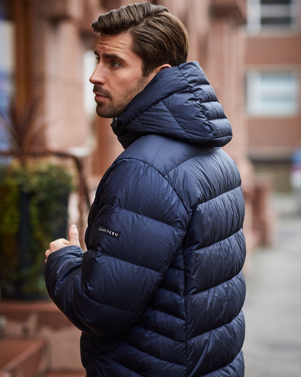 Mies seisoo kaupungilla ja katsoo taaksepäin yllään tummansininen Valto-kevytuntuvatakki (väri: yönsininen), jossa on huppu ja leveät vaakasuuntaiset tikkaukset. Hihassa on Joutsen-logomerkki.