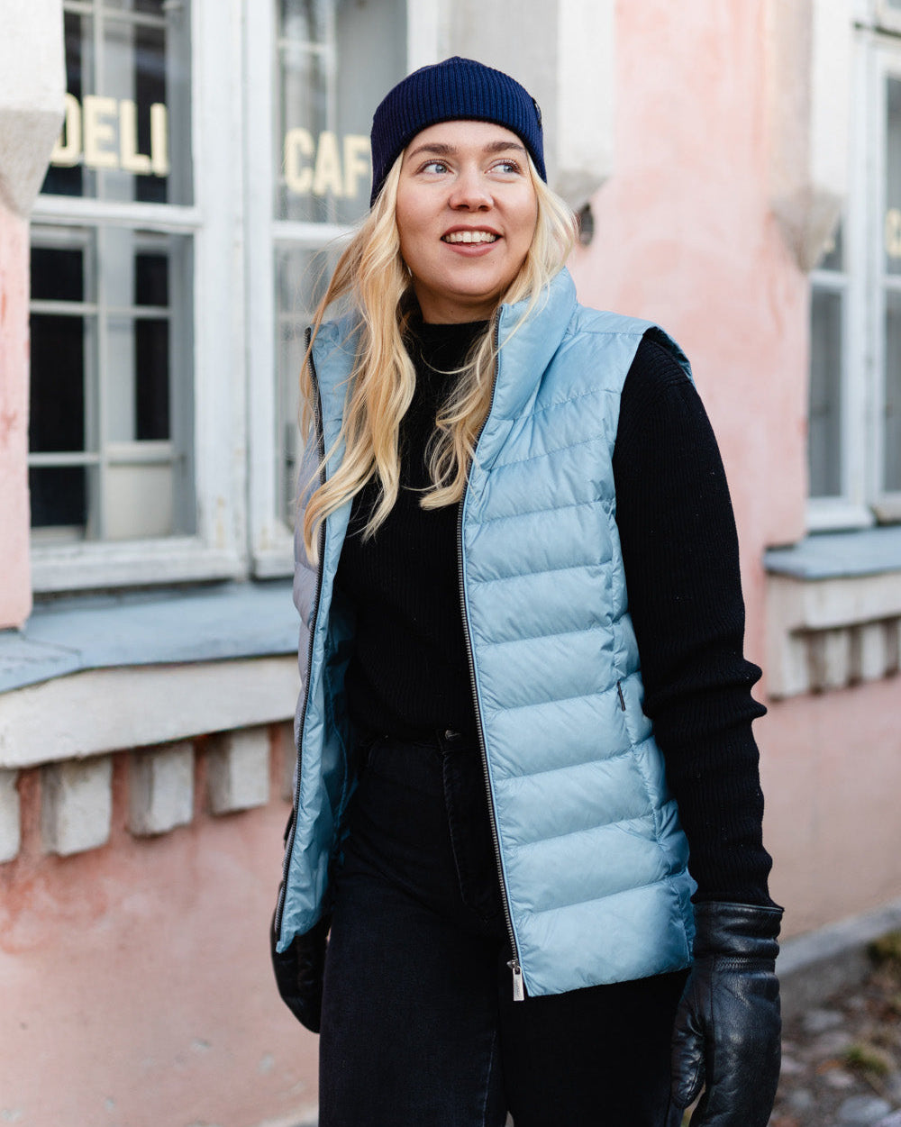 Nainen seisoo kadulla vaaleansinisessä Lady-untuvaliivissä, (väri: kissankello). Liivissä on vaakasuuntaiset tikkaukset ja kevyt kiilto. Hänellä on musta pipo, pooloneule, housut ja nahkahanskat.