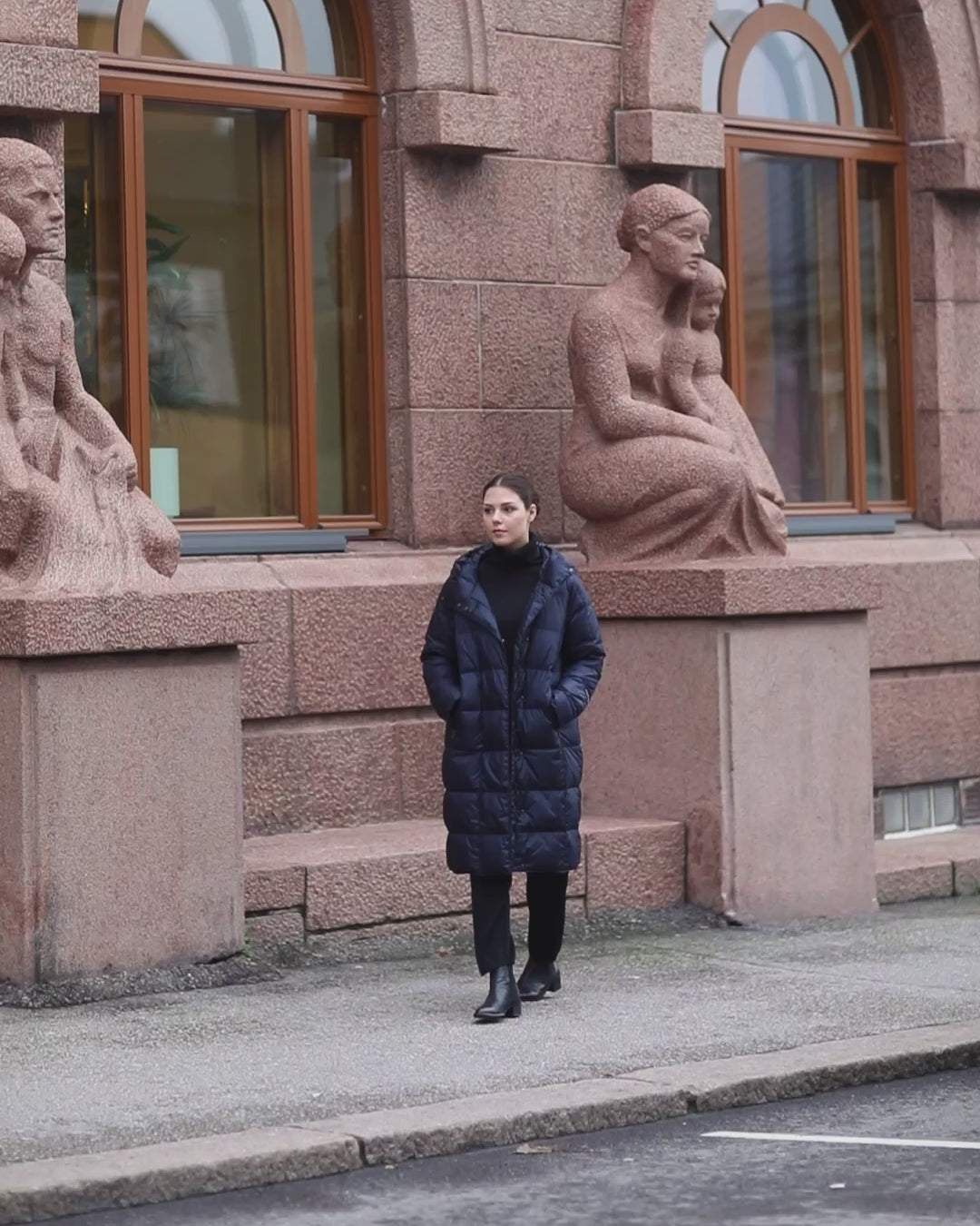 Nainen kävelee kaupungin kadulla ja asunnon parvekkeella pukeutuneena tummansiniseen pitkään ruututikattuun Essi-kevytuntuvatakkiin (väri: yönsininen).