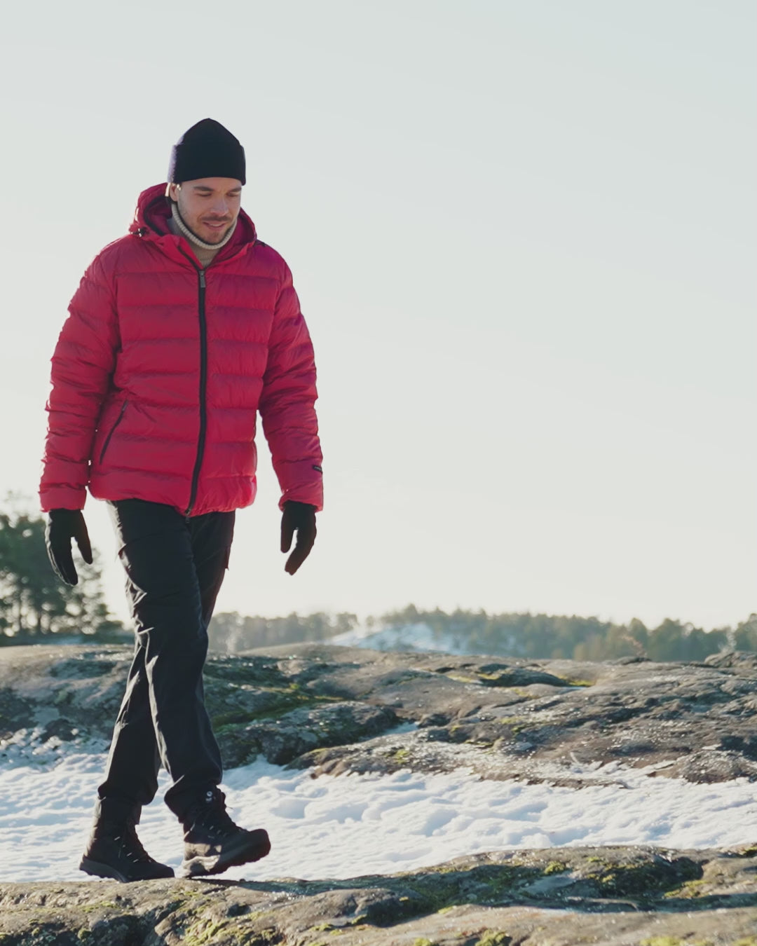 Henkilö kulkee talvisessa maisemassa yllään vadelman värinen Kuulas-kevytuntuvatakki. Hänellä on musta pipo, vaalea poolokaulus ja mustat hankasormikkaat. 